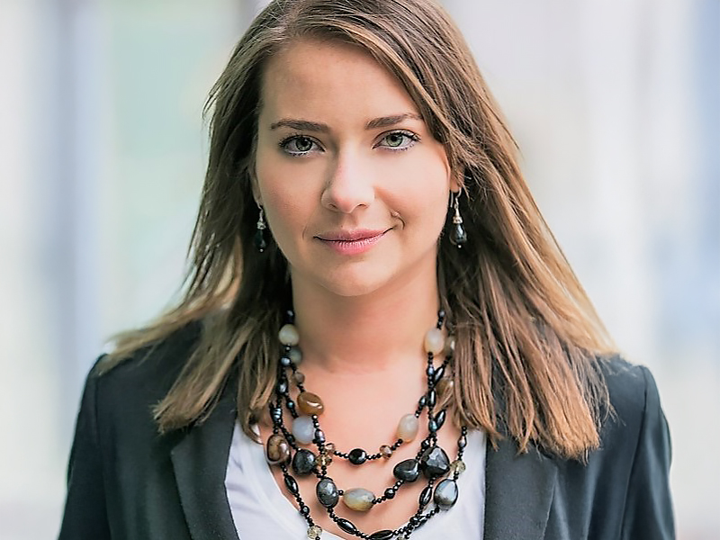 Miriam Clark headshot with her brown hair past her shoulders, a chunky wooden necklace and smiling at the camera
