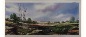A watercolour landscape painting of a wide-open field with rocky terrain and sparse greenery. A few tall, bare tree branches rise on the left, while clusters of green trees appear in the distance under a vast sky filled with soft purple and blue clouds. Signed in the corner with "Ensieh 2013."