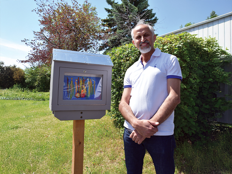 Fadi Alkhouri standing next to his North East Mini Gallery exhibition on a bright sunny day. The artwork is titled Community of Hope.