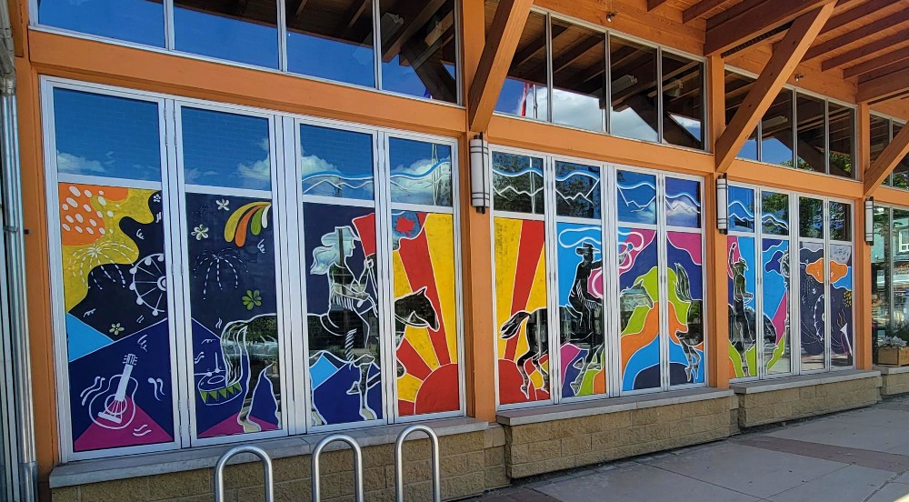 A wide spread of windows with wooden beams supporting an overhanging roof. On each of the windows is a display of bright artwork featuring themes for stampede.
