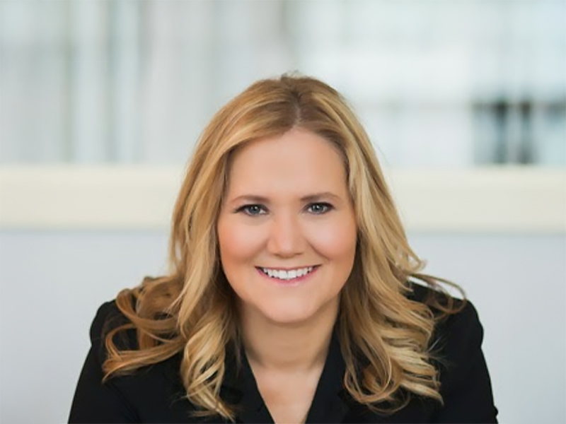 Lynn Moen looking straight ahead and smiling with blonde/brown hair and a dark top