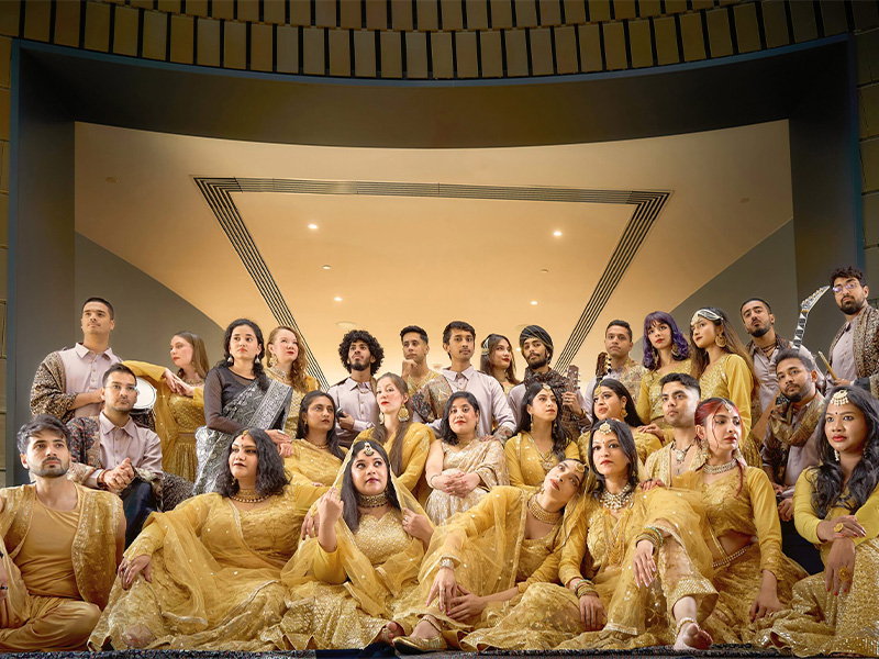 A group of people in traditional South Asian dress in the colour of gold/yellow, sitting and standing posing for a picture in a room
