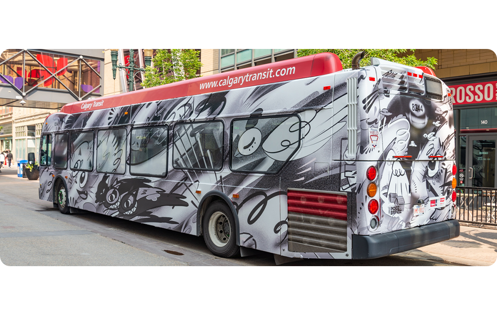 A Calgary Transit bus wrapped in black, white and grey comic-style characters with bold lines and expressive faces. It's parked downtown near Rosso Coffee Roasters.
