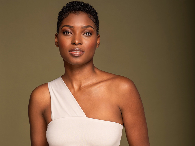 Sydonne Warren wearing a white, one-shouldered top against an olive-coloured background