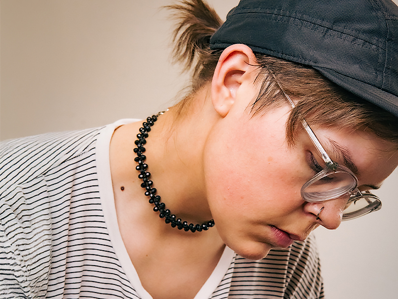 Blake McLeod wearing a cap, glasses and black necklace looking down to the right