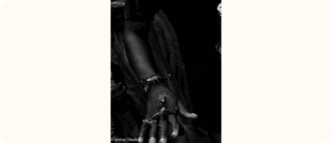 A black-and-white photo showing the outstretched hand of a person adorned with bracelets and holding small lizards or reptiles.