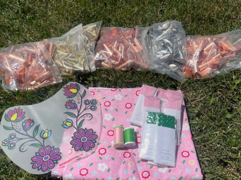 Fabric, thread and accessories for making Indigenous regalia are spread out on a patch of grass.