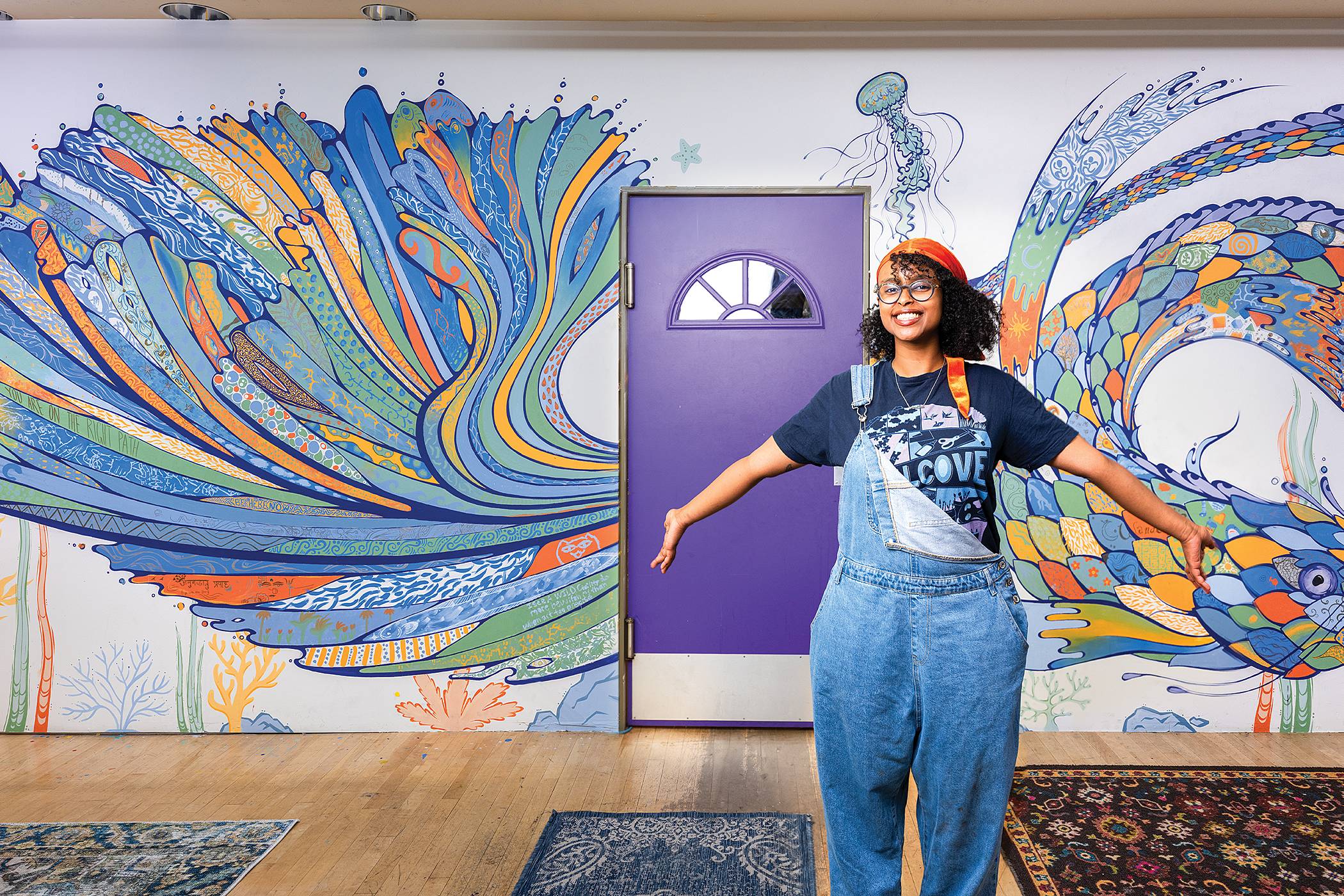 Artist Bethel Afework poses in front of her colourful artwork on a wall which includes a bright purple door.