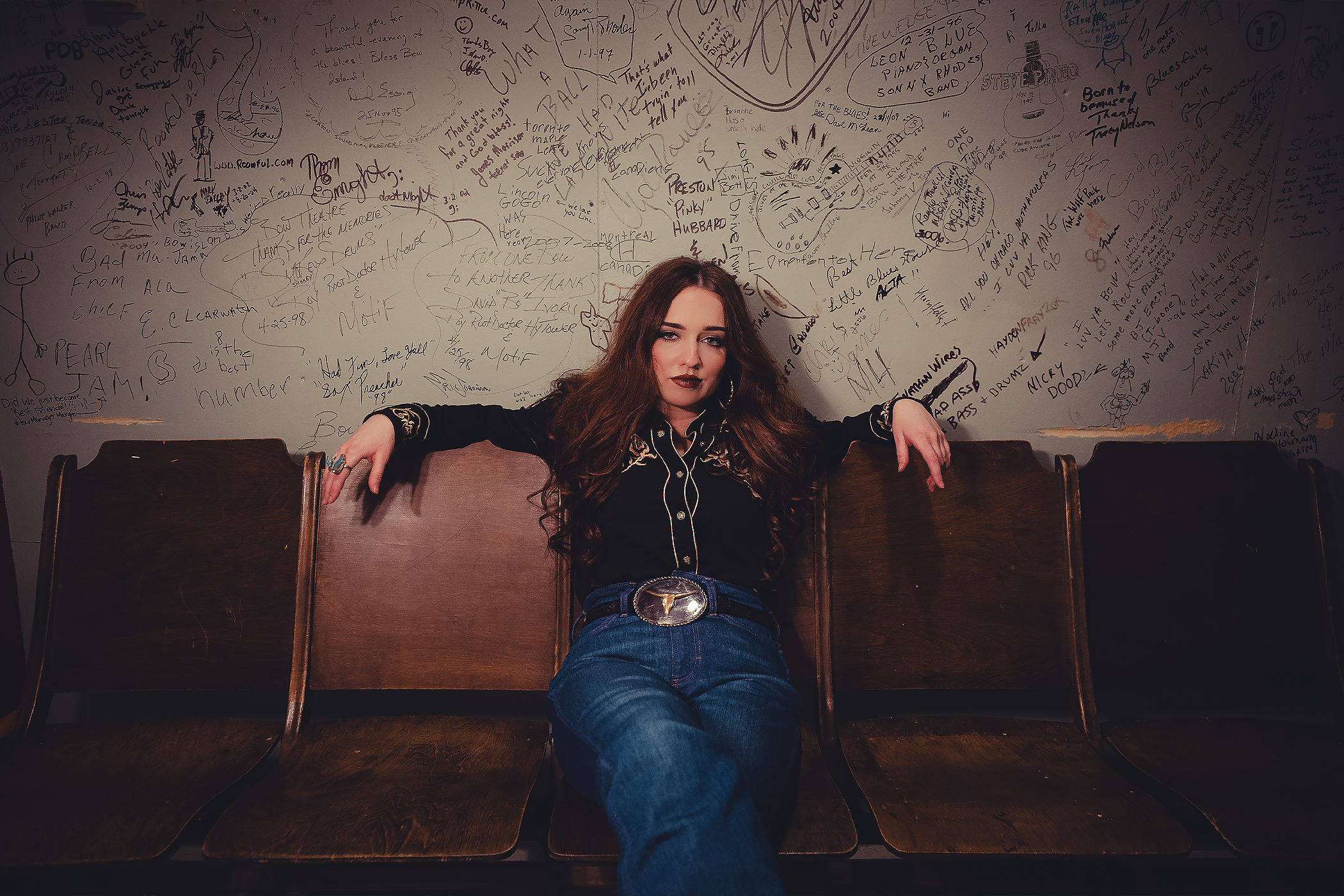 Noeline Hofmann sitting on a bench in front of a wall which is covered in marks and graffiti