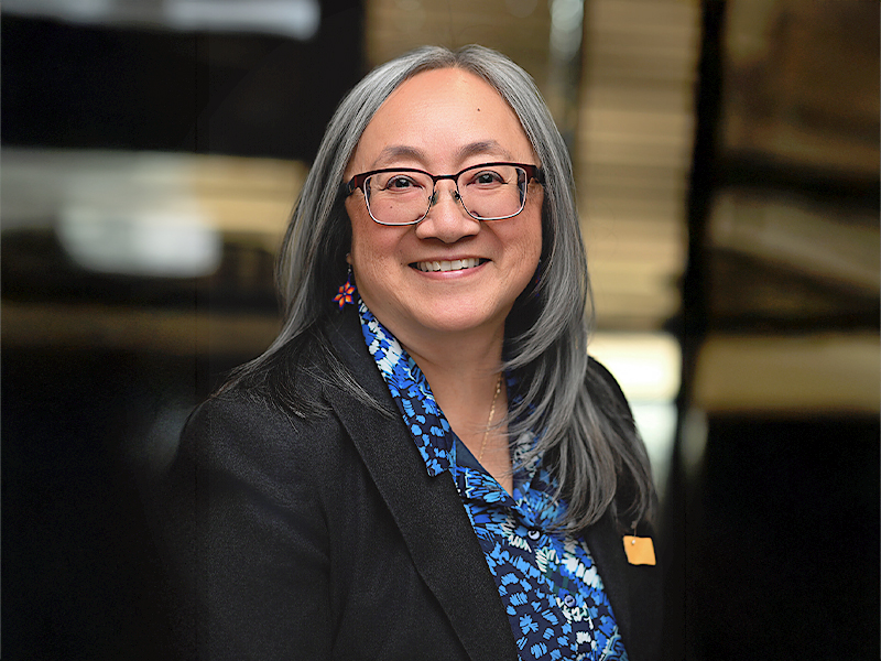 Patti Pon smiling with glasses on, looking forward, waearing a blue shirt and black blazer