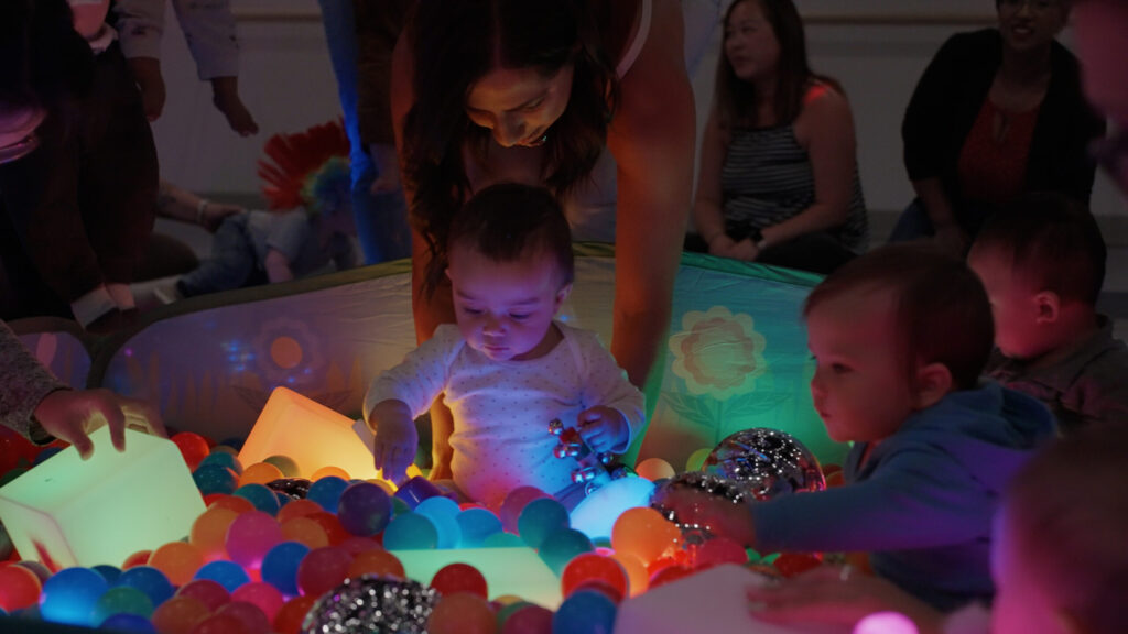 A bunch of kids with with what appears to be parents, playing in a glowing ball pit.