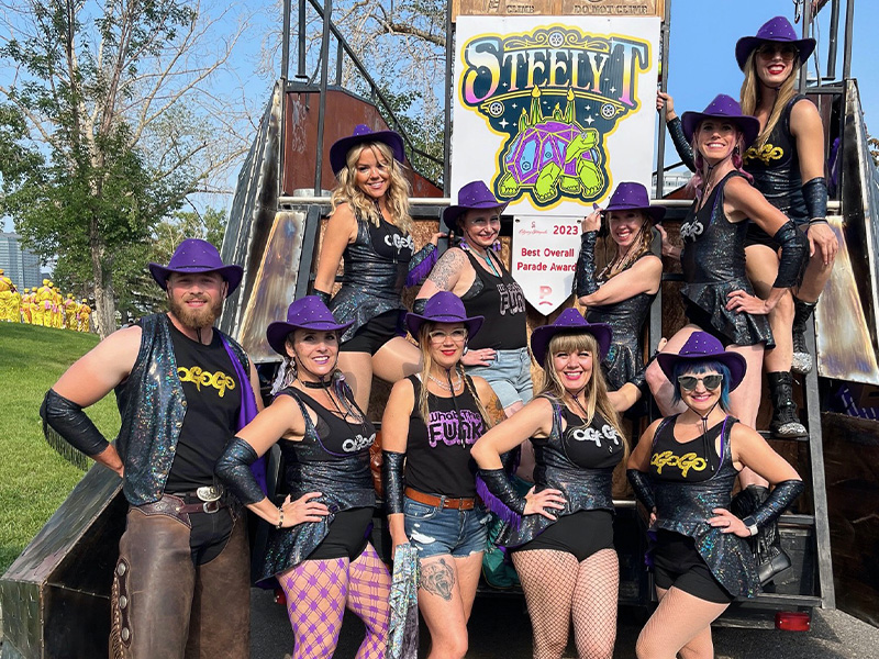 Ten people wearing purple hats and faux western gear standing outside in front of a mobile stage