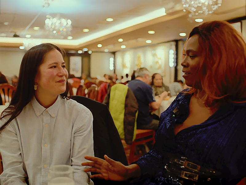 Gillian McKercher and Adora Nwofor sit at a table at a restaurant facing each other in discussion