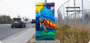 A utility box painted with a colourful underwater scene featuring a sea turtle swimming through blue and green waves, with a bright sun.