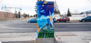 A utility box painted with a bright cityscape at the bottom, airplanes and clouds in the middle, and a rocket and planets in space at the top.