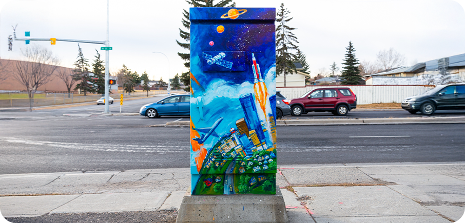A utility box painted with a bright cityscape at the bottom, airplanes and clouds in the middle, and a rocket and planets in space at the top.