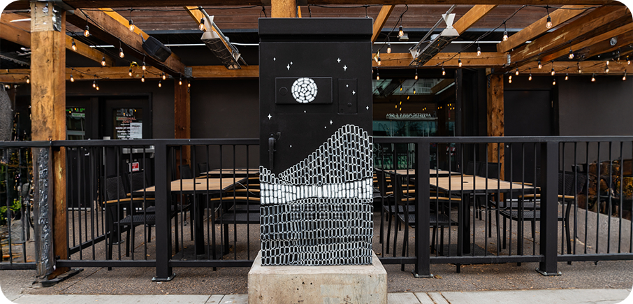 A utility box painted black with a white moon and stars above a wavy pattern made of small rectangular shapes.
