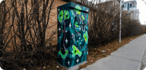 A utility box painted with floating green frogs, stars, and swirling shapes on a dark teal background.