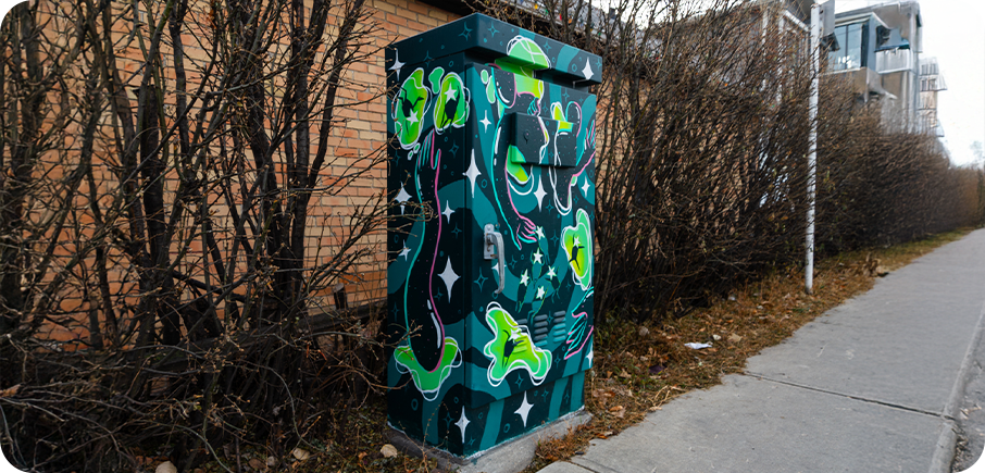 A utility box painted with floating green frogs, stars, and swirling shapes on a dark teal background.
