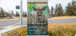A utility box painted with a realistic deer peeking through tall green and brown grass.