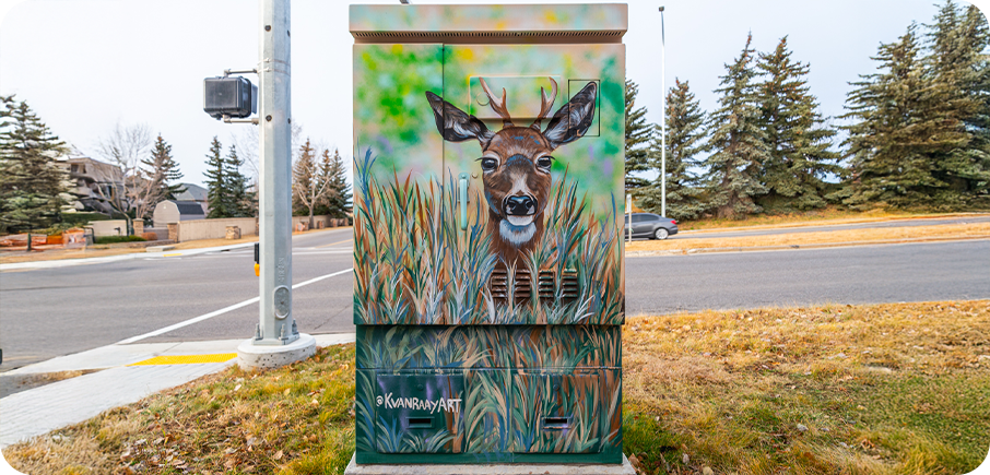 A utility box painted with a realistic deer peeking through tall green and brown grass.