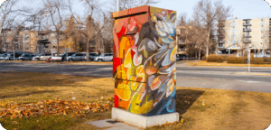 A utility box painted with bold, swirling shapes in warm reds, yellows, and oranges blended with cooler blues and purples, creating an abstract, colourful pattern.