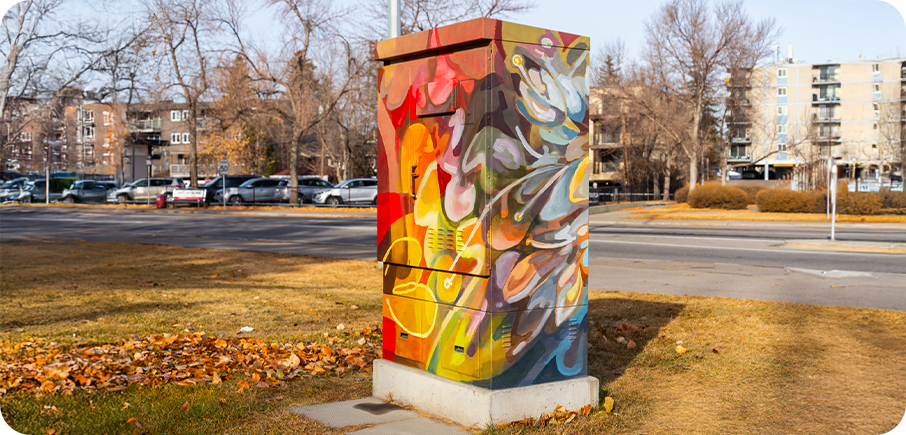 A utility box painted with bold, swirling shapes in warm reds, yellows, and oranges blended with cooler blues and purples, creating an abstract, colourful pattern.