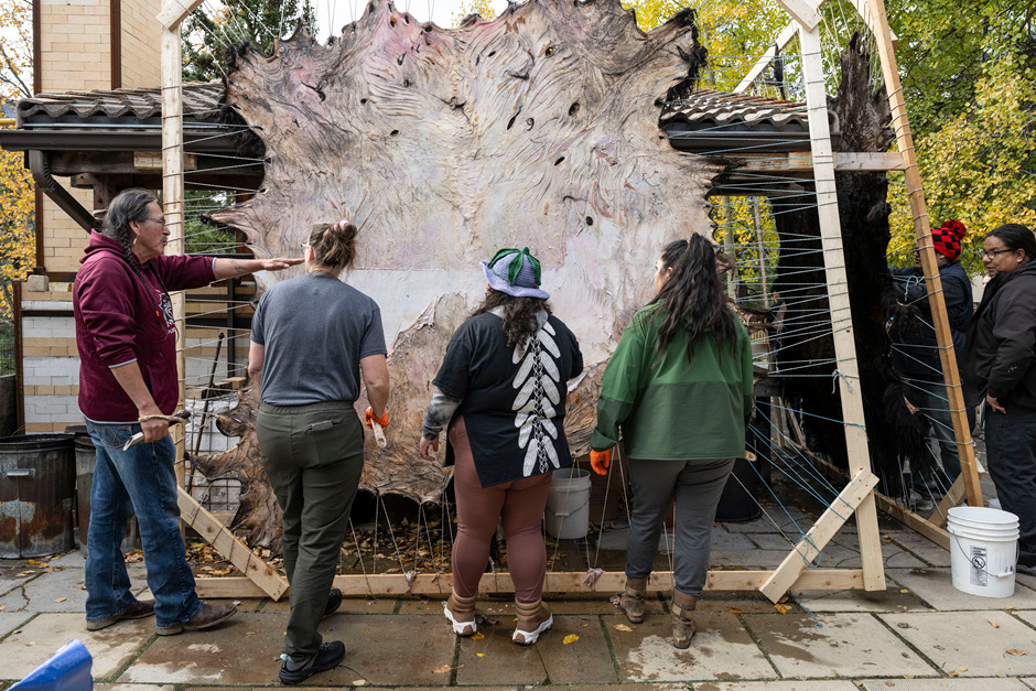 A group of people being instructed in front of a large animal hide or pelt in a frame of wood.