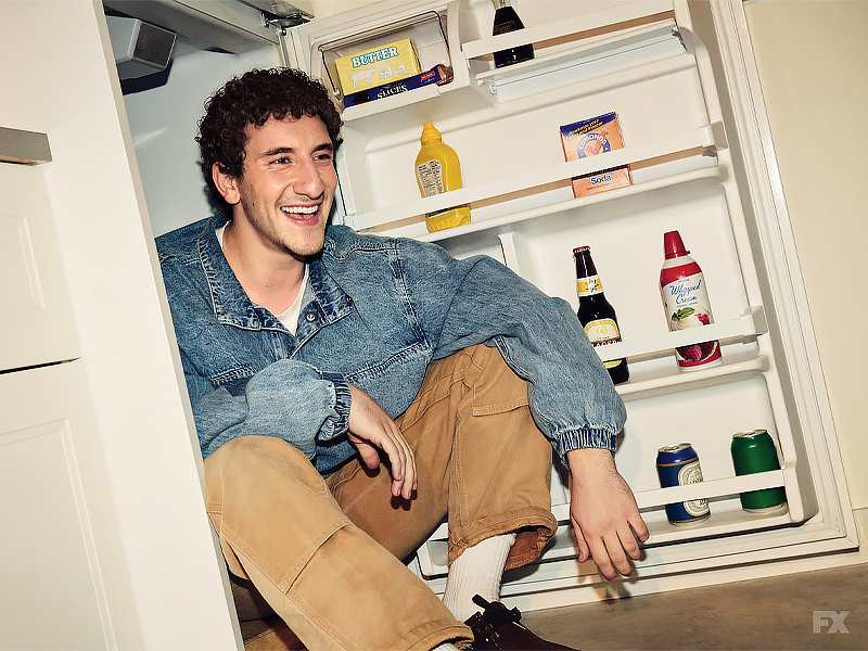 A photo of comic Malik Elassal sitting inside a refrigerator smiling warmly