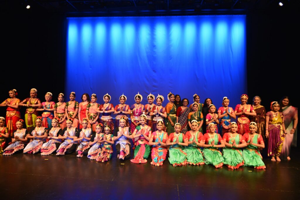 Group photo of performers in Indian cultural attire on stage